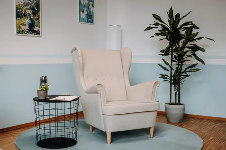Heller Sessel in ruhigem Praxisraum mit Zimmerpflanze und kleinem Tisch, ideal für Psychotherapie-Sitzungen.