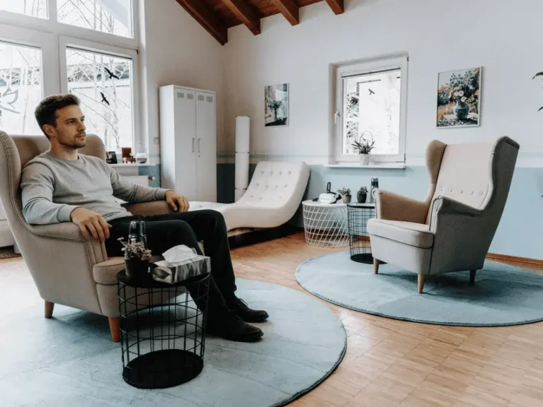 Mann sitzt in einer hellen, gemütlichen Praxis mit Sesseln und Pflanzen, einladend für Psychotherapie.