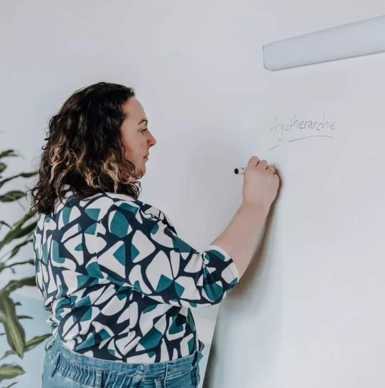 Frau schreibt auf Whiteboard, im Hintergrund eine Taubenzeichnung an der Wand.